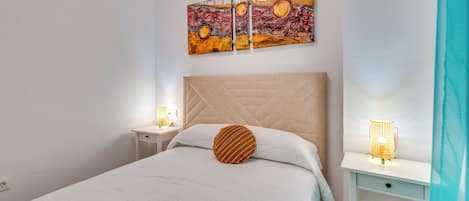 A bedroom with a bed, a nightstand, a bedside lamp, and a wall-mounted artwork.