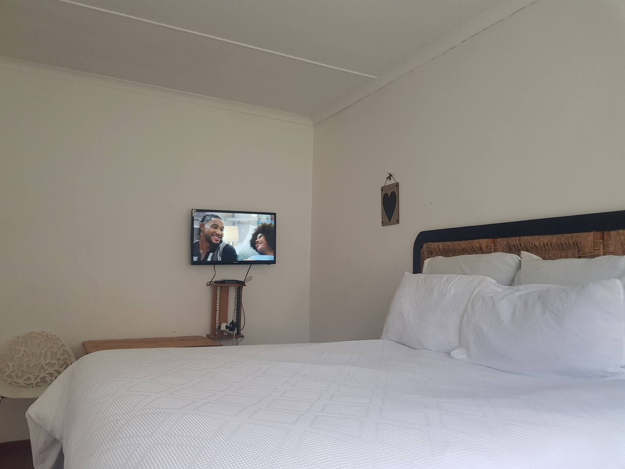A bedroom with a bed, a television mounted on the wall, and a small bedside table.