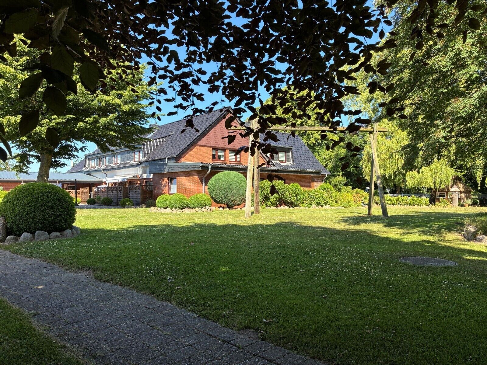 A two-story house with a well-maintained lawn, a round hedge, and a brick exterior.