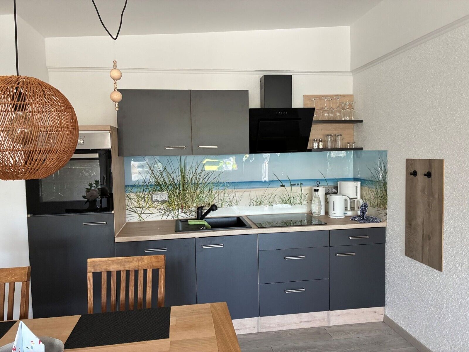 Eine moderne Küche mit dunklen Schränken, einem großen Fenster und einem Essbereich mit einem Holztisch und Stühlen.