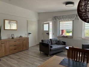 Ein modernes Wohnzimmer mit einem grauen Sofa, einer Holztruhe und einem Essbereich mit Tisch und Stühlen.