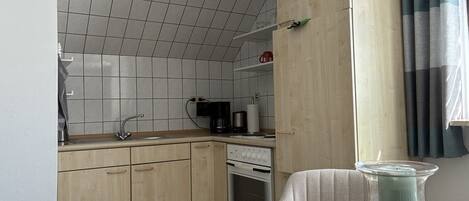 A compact kitchen with a tiled backsplash, a sink, a coffee maker, and a stove.