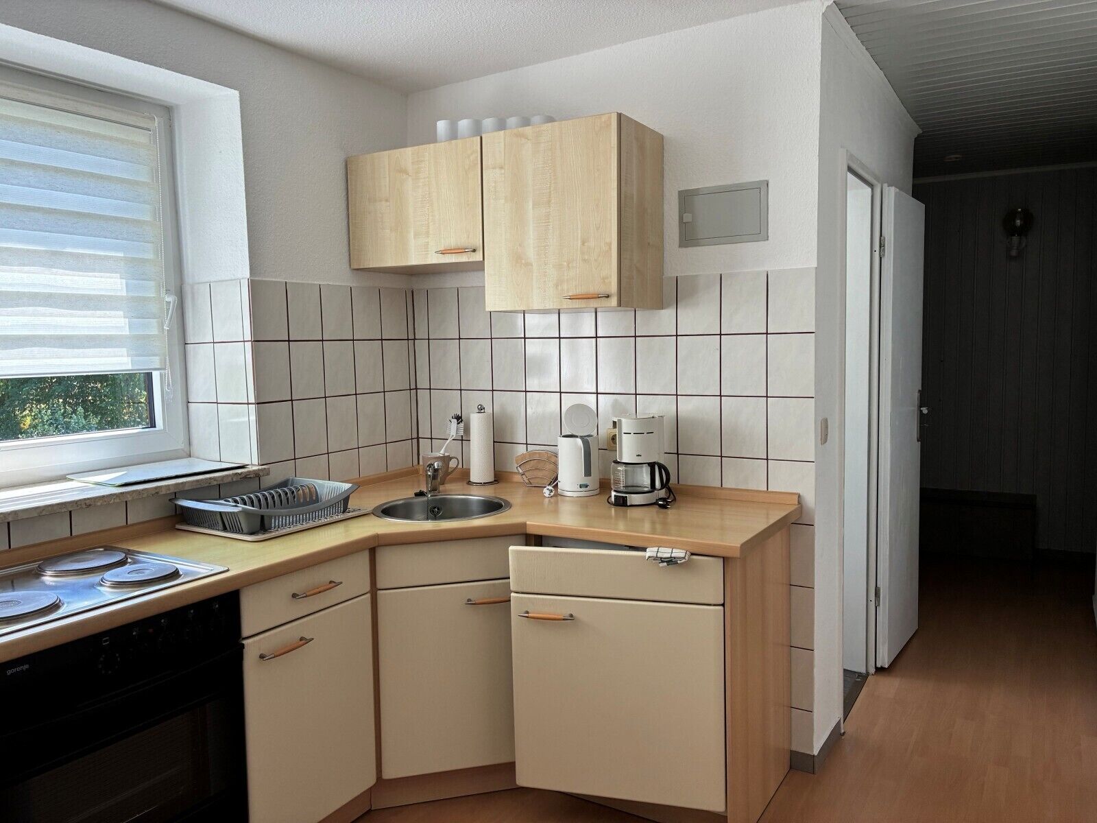 Pieni, käytännöllinen keittiö, jossa on liesi, pesuallas ja puiset kaapit.