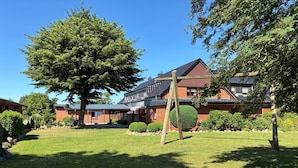 A building with a brick facade, a large lawn, and a tree. - Hans' Vacation Rental Near the Baltic Sea with a Natural Garden (Waabs)