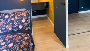 Quarto com cama, luminária de cabeceira e vista para um banheiro com pia e espelho.
