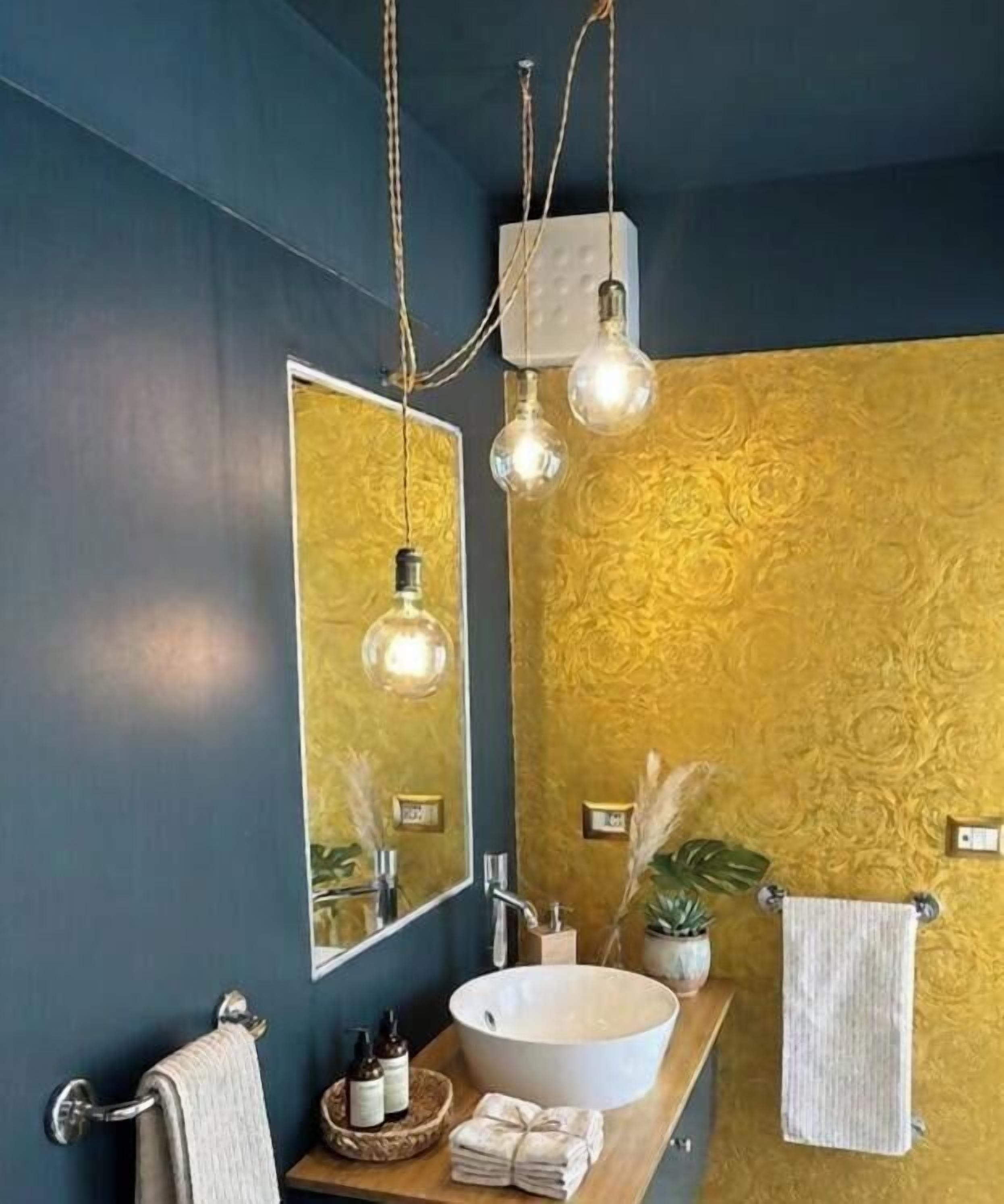 A bathroom with a large mirror, a round sink, and a gold-patterned wall.