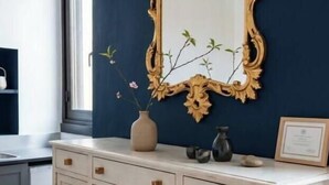 Um quarto com um espelho grande e ornamentado na parede, um armário branco embaixo e um vaso com flores sobre o armário.