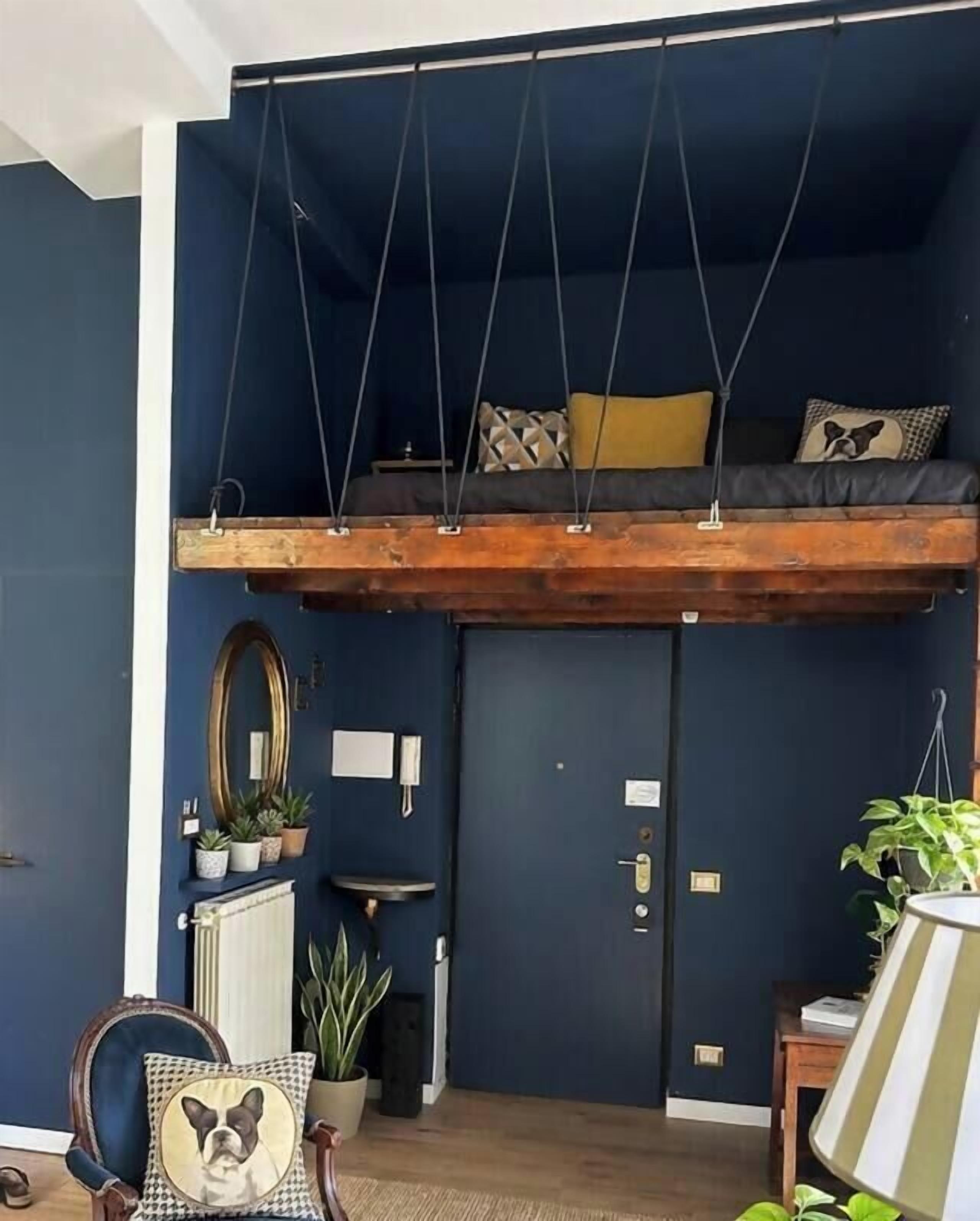 Une pièce avec un lit en mezzanine, un miroir, une chaise avec un coussin et une lampe.