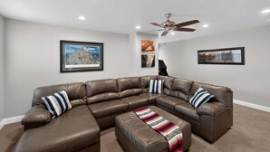 A modern living room with a sectional sofa, a ceiling fan, and framed artwork on the walls. - Casa Encantada | Pool, Pickleball, Near Zion (Washington)