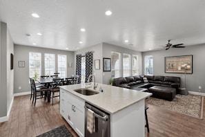 A modern kitchen with a central island, a dining area with chairs, a living room with a sofa, and a ceiling fan. - Casa Encantada | Pool, Pickleball, Near Zion (Washington)