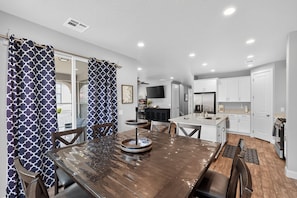 A modern kitchen with white cabinets, a stainless steel refrigerator, and a dining area with a wooden table and chairs. - Casa Encantada | Pool, Pickleball, Near Zion (Washington)