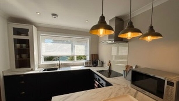 A modern kitchen with pendant lighting, a microwave, and a marble countertop. - Cosy two Bedroom Bungalow With Garden in Ballater (Ballater)