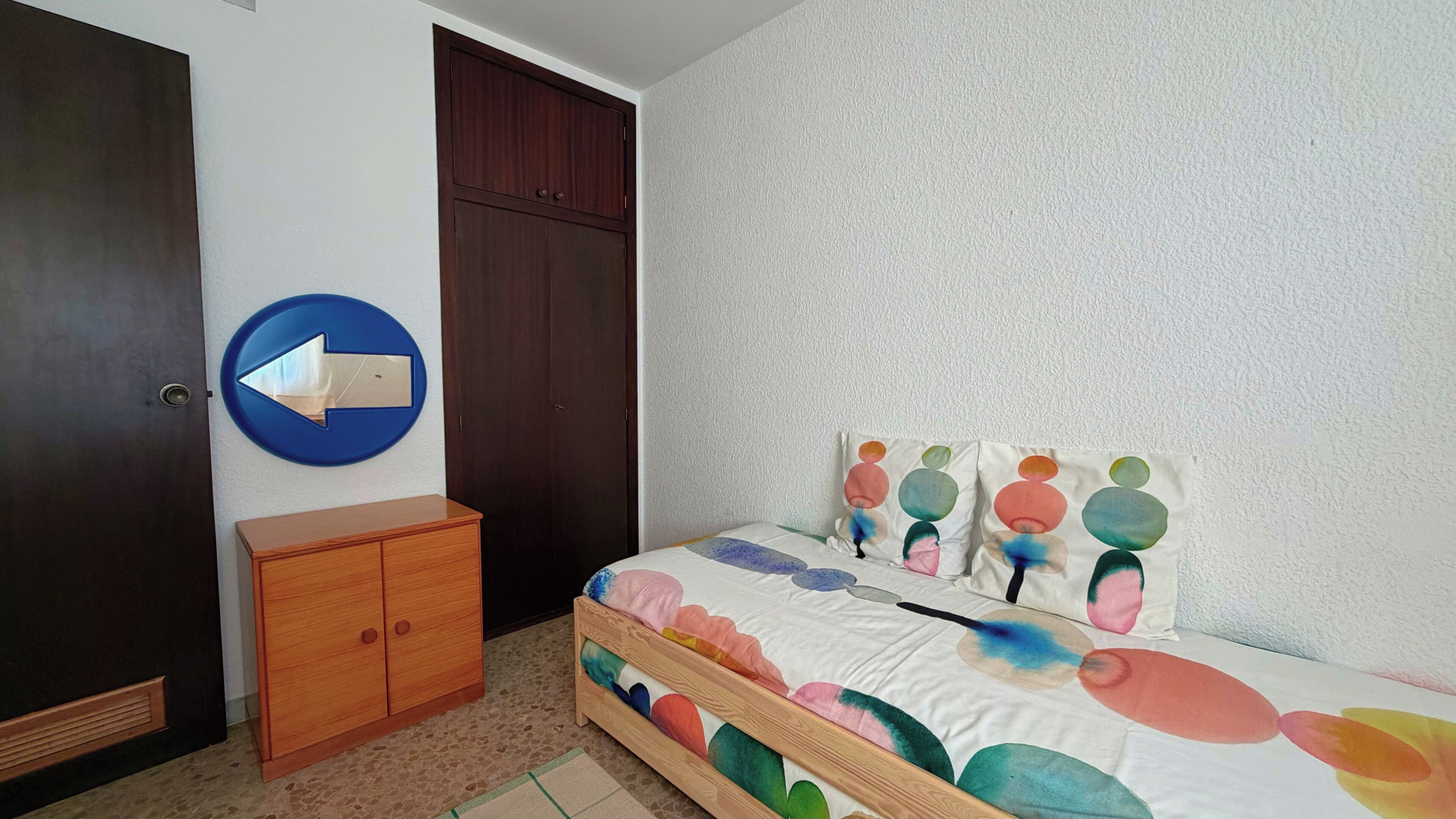 Un dormitorio con cama, armario, puerta y un letrero circular sujeto a la pared.