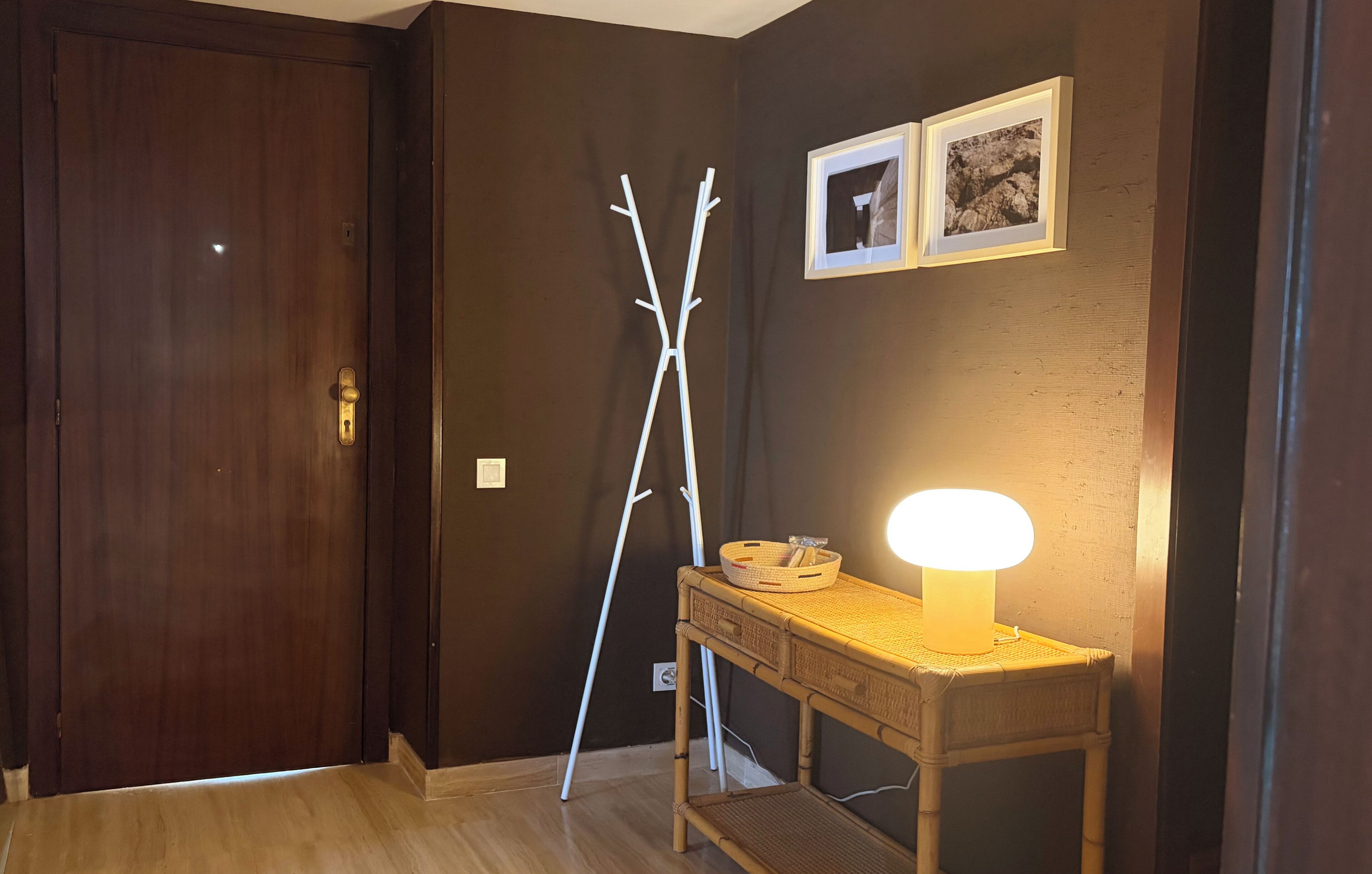 A wooden door, a white metal stand, a wall-mounted picture frame, and a table with a lamp.