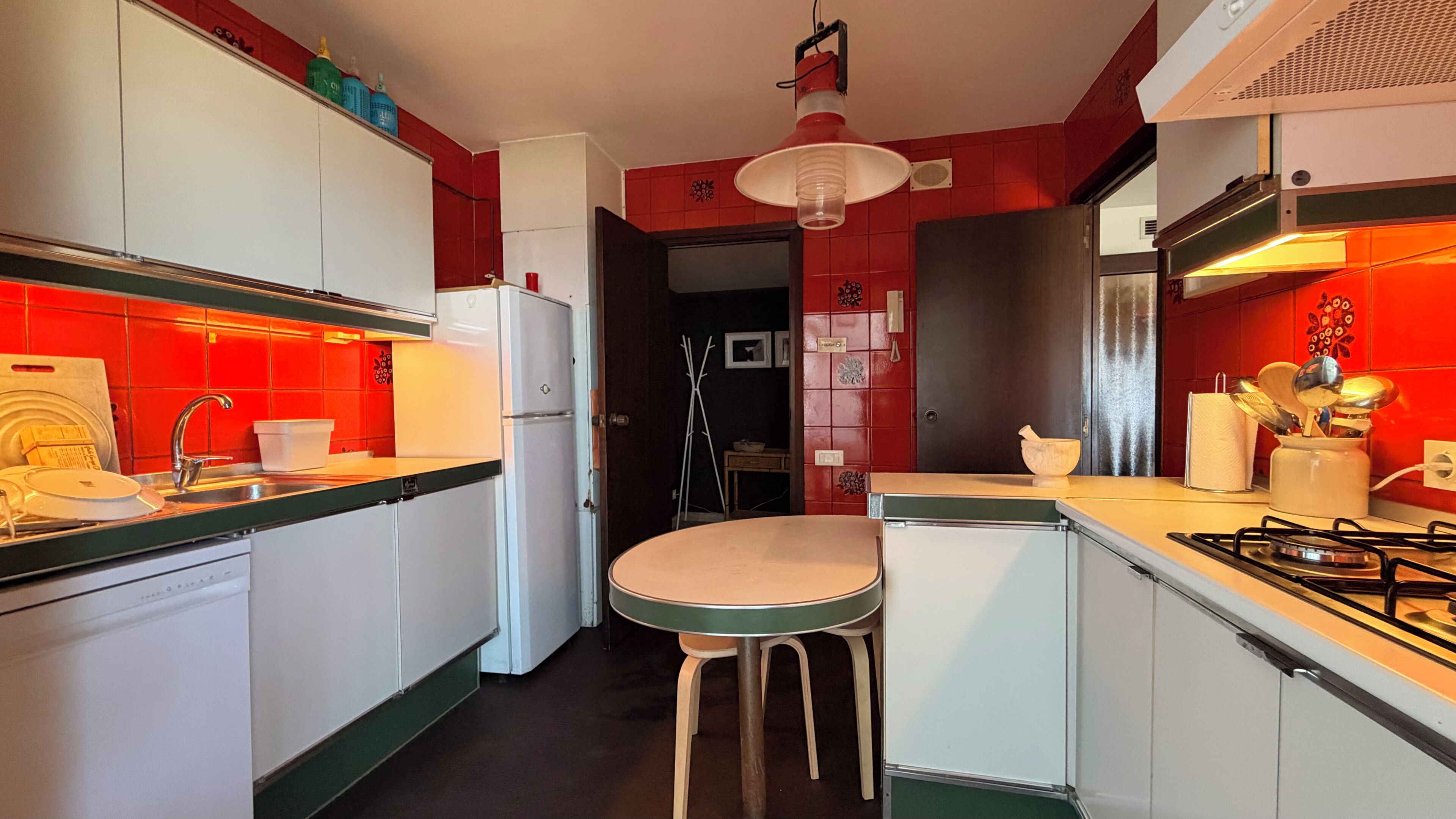 A compact kitchen with a central island, white appliances, and red accents.