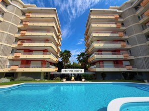 Ein Hotel mit Schwimmbad, mehreren Balkonen und blauem Himmel.