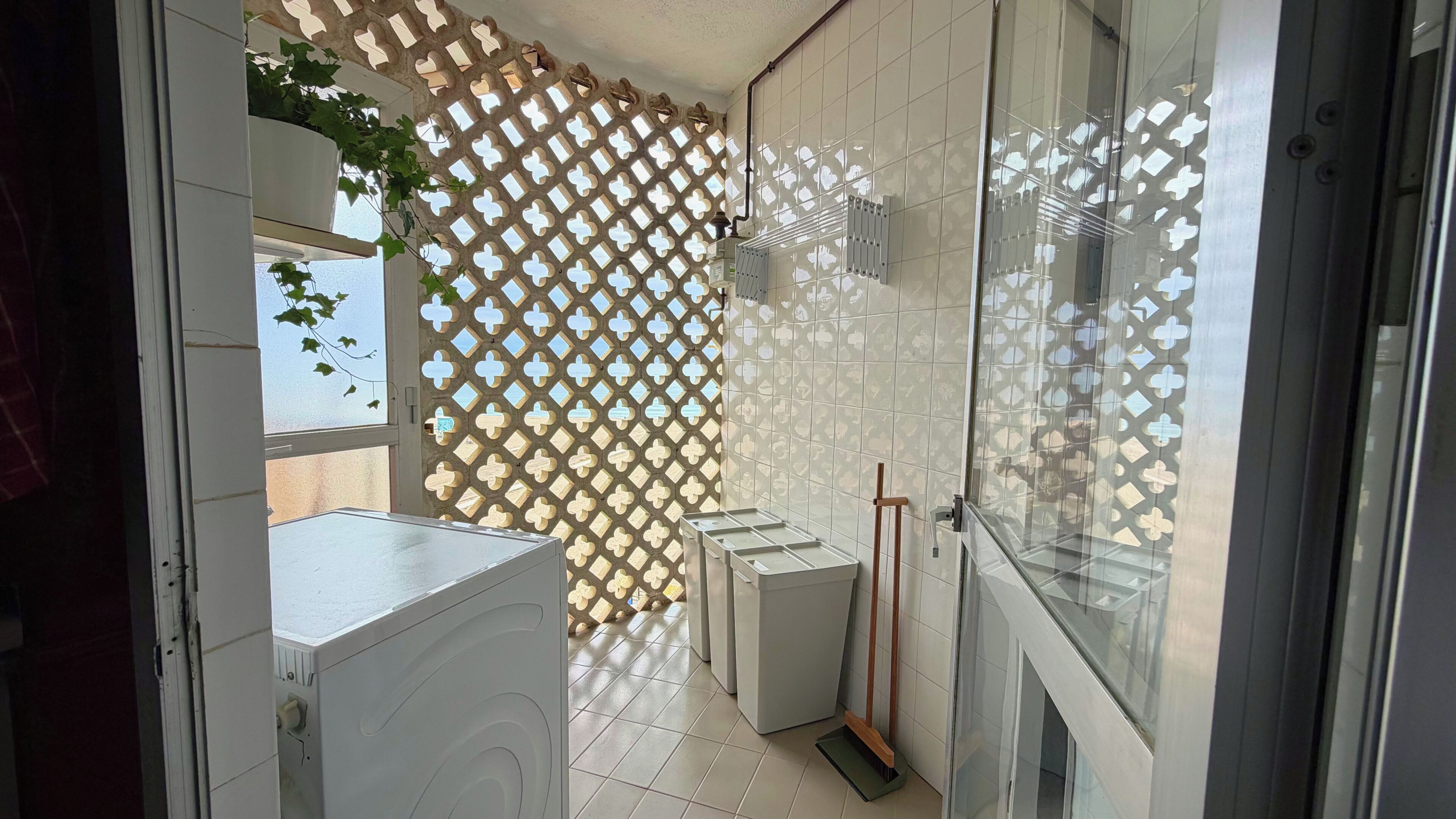 Une salle de bain avec un sol carrelé, un espace douche doté de portes en verre, un lavabo blanc et un mur décoratif orné d’un motif en treillis.