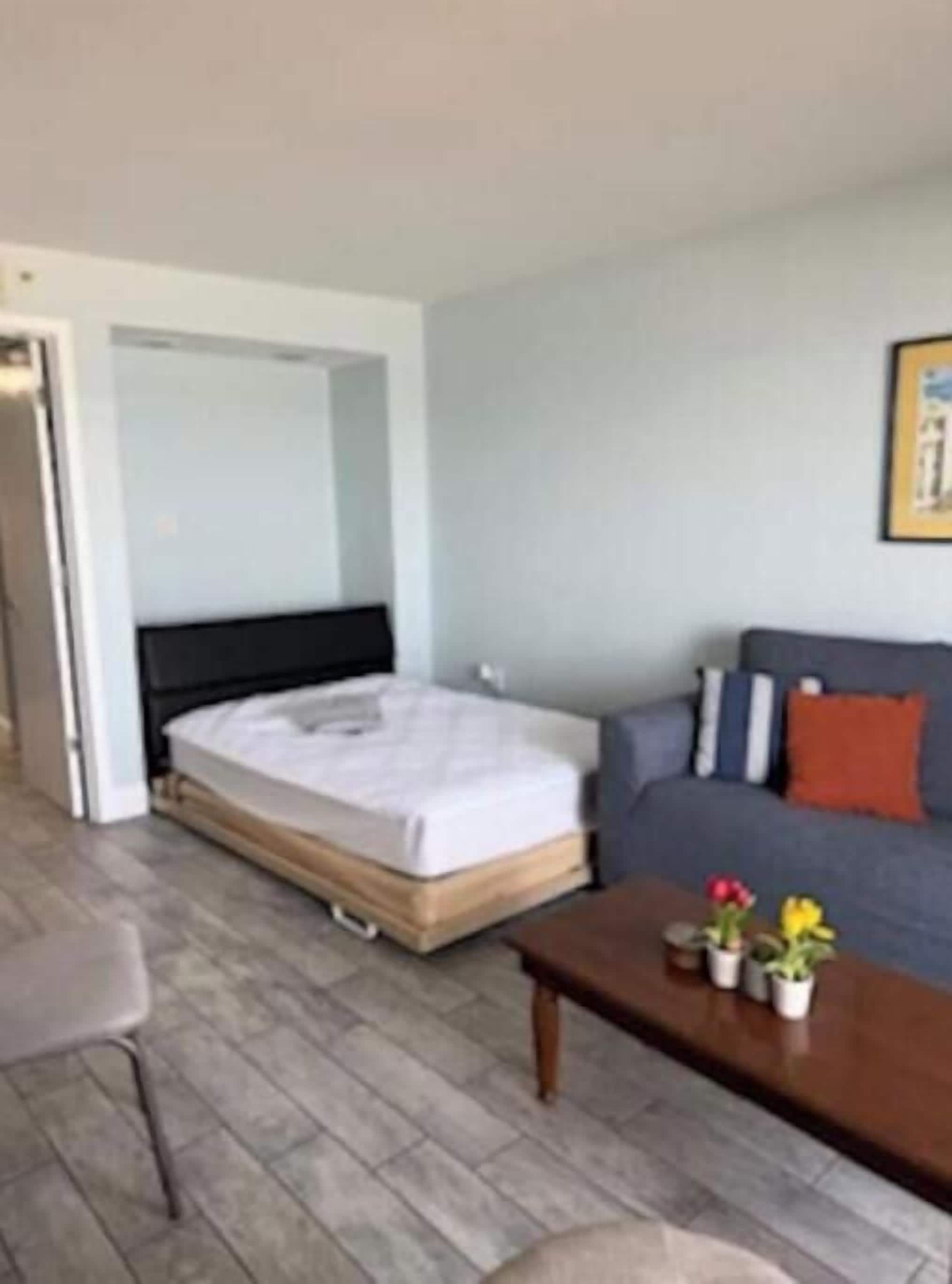 A room with a bed, a sofa, a coffee table with flowers, and a door leading to another room.