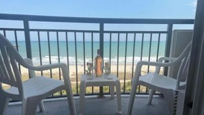 A balcony with two white plastic chairs and a small table, overlooking a beach. - At the heart of Myrtle Beach Oceanfront Condo (Myrtle Beach)