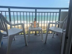 A balcony with two white plastic chairs and a small table, overlooking a beach. - At the heart of Myrtle Beach Oceanfront Condo (Myrtle Beach)