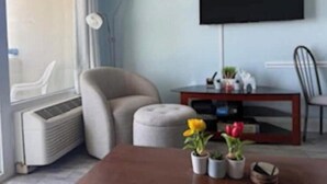 A living room with a flat-screen TV mounted on the wall, a sofa, a coffee table with potted plants, and a window with blinds. - At the heart of Myrtle Beach Oceanfront Condo (Myrtle Beach)