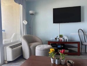 A living room with a flat-screen TV mounted on the wall, a sofa, a coffee table with potted plants, and a window with blinds. - At the heart of Myrtle Beach Oceanfront Condo (Myrtle Beach)