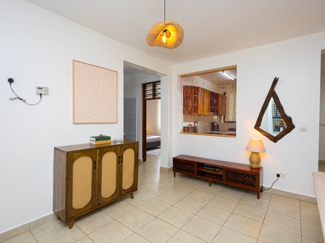 Une pièce comprenant un meuble en bois, un miroir, une lampe et un luminaire en matière tressée.
