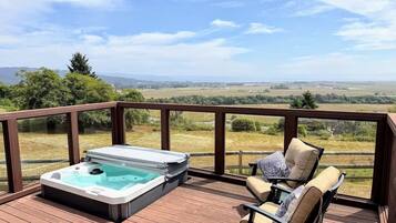 A hot tub on a wooden deck with a view of a rural landscape.