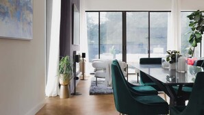 A modern dining area with a glass table, green chairs, and a view through large windows. - South Congress - Walk to SXSW, Downtown, ACL (Austin)