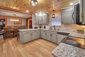 A kitchen with granite countertops, grey cabinets, wooden flooring, and a dining area with wooden chairs. - Luxury Living in the Smoky Mountains (Sevierville)