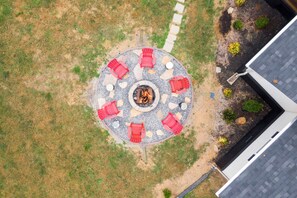 Luchtbeeld van een rond zitgedeelte buiten, met rode stoelen rond een centraal vuurkorf.