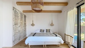A bedroom with a bed, wooden beams, a woven light fixture, and a view through a glass door. - Stunning new home in La Clere, Noirmoutier, with 6 bedrooms, 100 meters from the beach (Noirmoutier-en-l'Île)