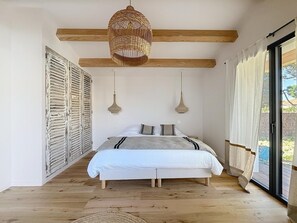 A bedroom with a bed, wooden beams, a woven light fixture, and a view through a glass door. - Stunning new home in La Clere, Noirmoutier, with 6 bedrooms, 100 meters from the beach (Noirmoutier-en-l'Île)