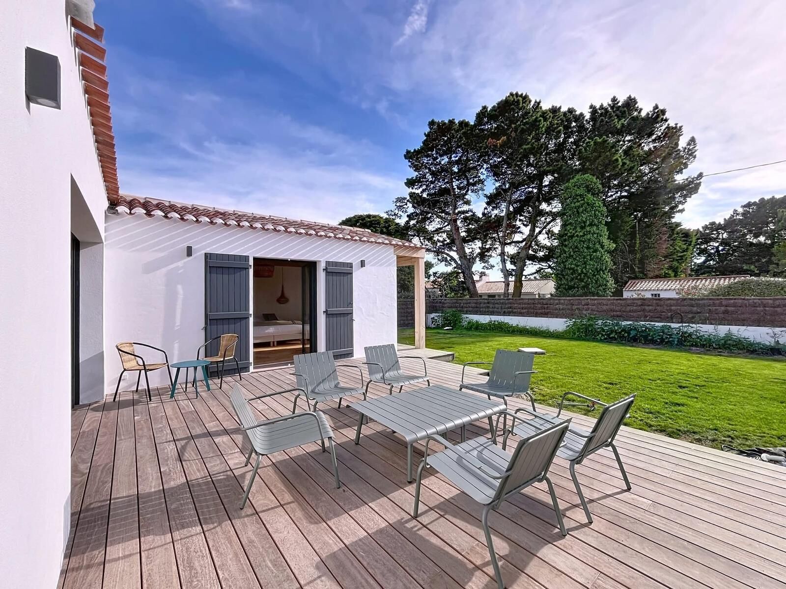 A covered patio with a table and chairs, a small open room with a bed, and a grassy yard with trees.