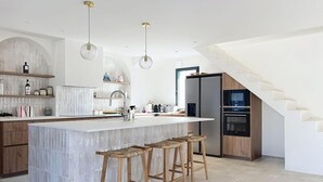 A modern kitchen with a central island, wooden stools, and a staircase. - Stunning new home in La Clere, Noirmoutier, with 6 bedrooms, 100 meters from the beach (Noirmoutier-en-l'Île)