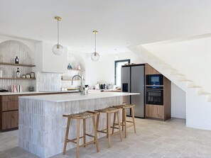 A modern kitchen with a central island, wooden stools, and a staircase. - Stunning new home in La Clere, Noirmoutier, with 6 bedrooms, 100 meters from the beach (Noirmoutier-en-l'Île)