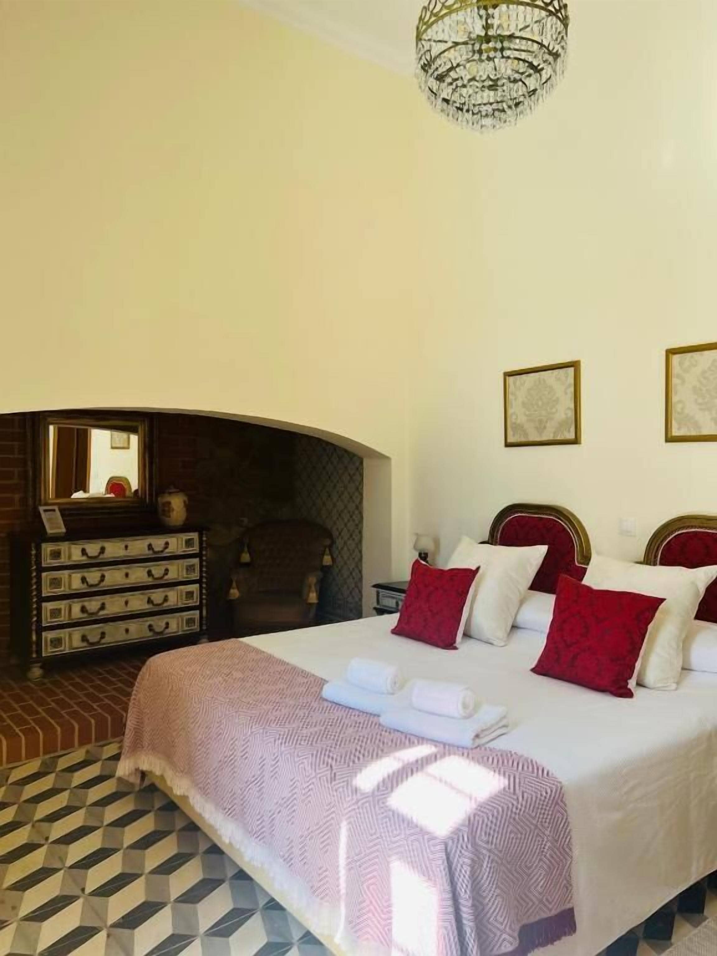 A hotel room with a bed, a dresser, a fireplace, and framed pictures on the wall.