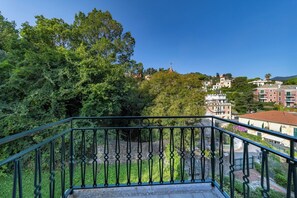 A balcony with a wrought iron railing overlooking a lush green area with trees and buildings in the background. - Villa with ocean views, large garden, close to the harbor, downtown, and the beach (Rapallo)