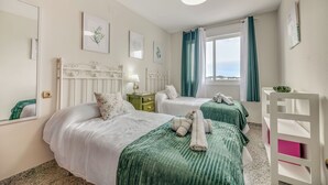 Une chambre d’hôtel avec deux lits, une table de chevet, une commode, une fenêtre avec des rideaux et des œuvres d’art accrochées aux murs.