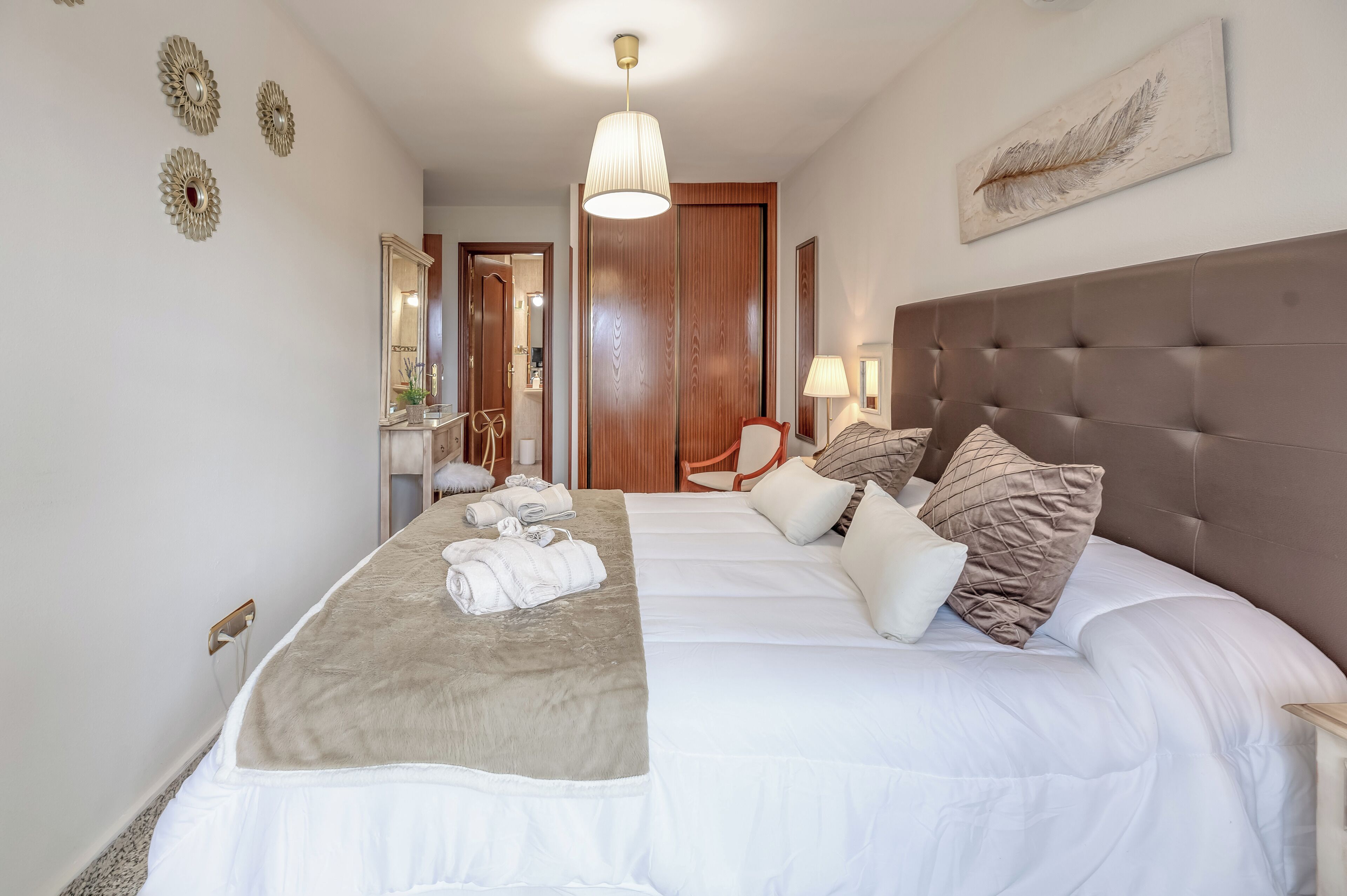 A hotel room with a large bed, a chair, a mirror, and a door leading to a bathroom.