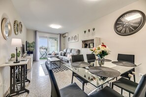 A modern living room with a sofa, dining table, chairs, and a large wall clock. - LXR Jazmines 2-Bedroom, Downtown (Fuengirola)