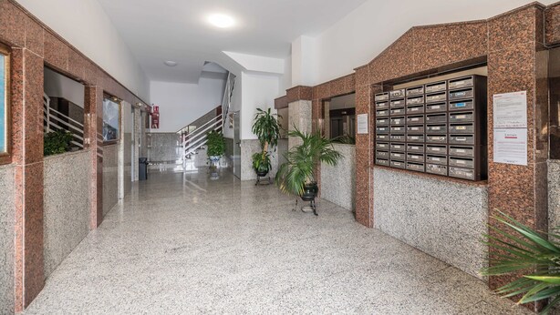 Un hall d’entrée avec un sol en marbre, un escalier et une rangée de boîtes aux lettres.