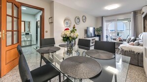 Un salon moderne avec une table à manger en verre, des chaises noires, un canapé agrémenté d’un plaid blanc et une vue sur la ville grâce à une grande fenêtre.