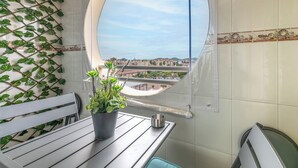 Un balcon donnant sur un paysage urbain, une plante en pot, une tasse en métal et un banc.