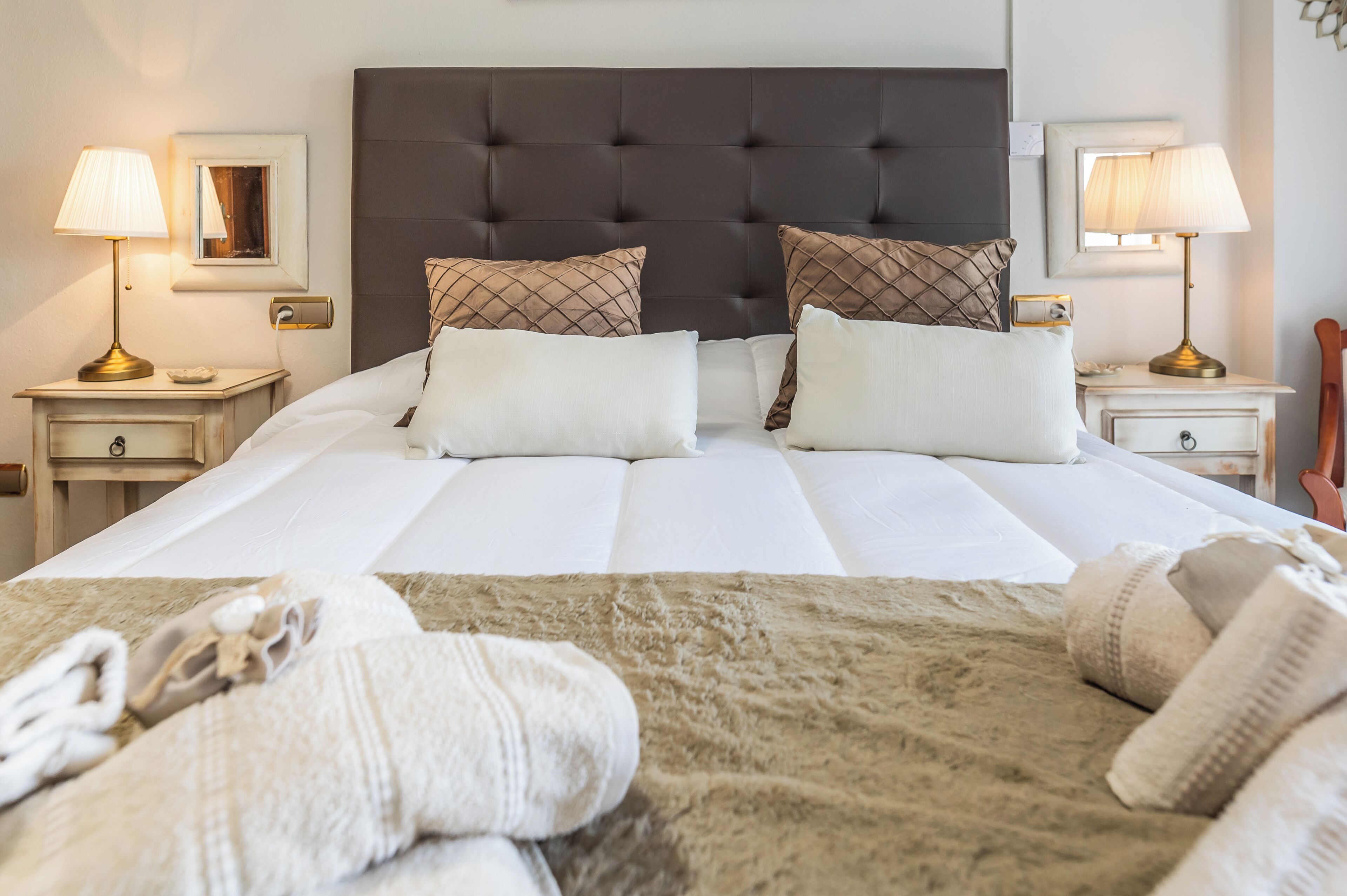 A neatly made bed with a tufted headboard, two bedside tables with lamps, and a fluffy throw blanket on the bed.