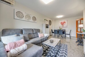A modern living room with a grey sofa, a coffee table, and a dining area with chairs and a table. - LXR Jazmines 2-Bedroom, Downtown (Fuengirola)
