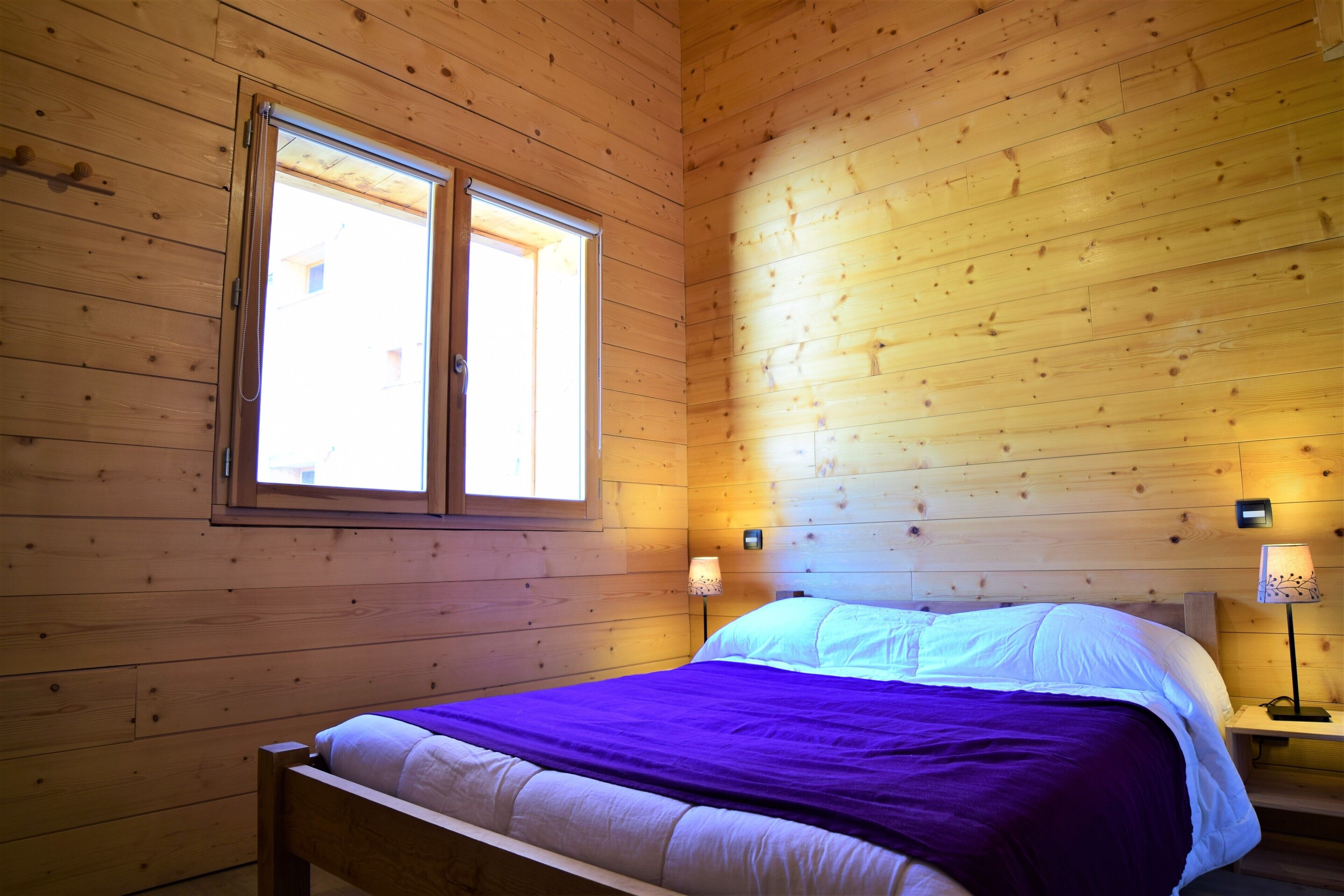 A wooden-paneled room with a bed, two bedside lamps, and a window.