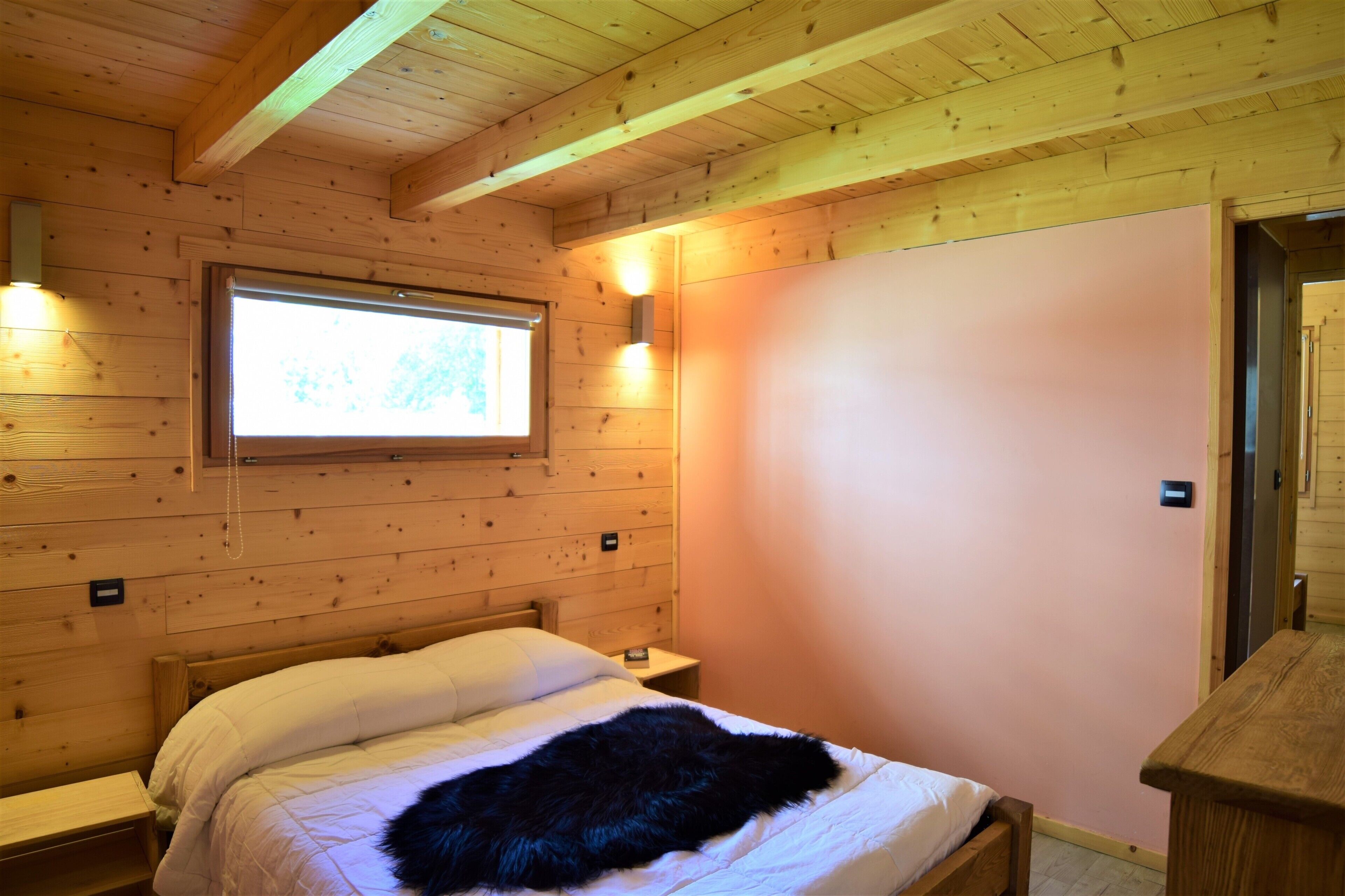 A wooden cabin room with a bed, a nightstand, a window, and a door.