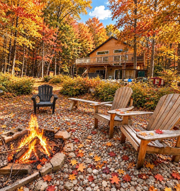 A cabin with a fire pit surrounded by Adirondack chairs and a wooden deck.