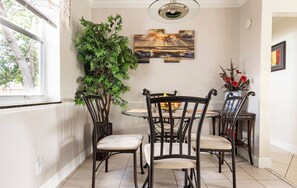 A dining area with a round table, four chairs, a potted plant, a wall-mounted artwork, and a vase with flowers. - 3BR Home Near Fort Lauderdale Beach | Sleeps 5 (Fort Lauderdale)